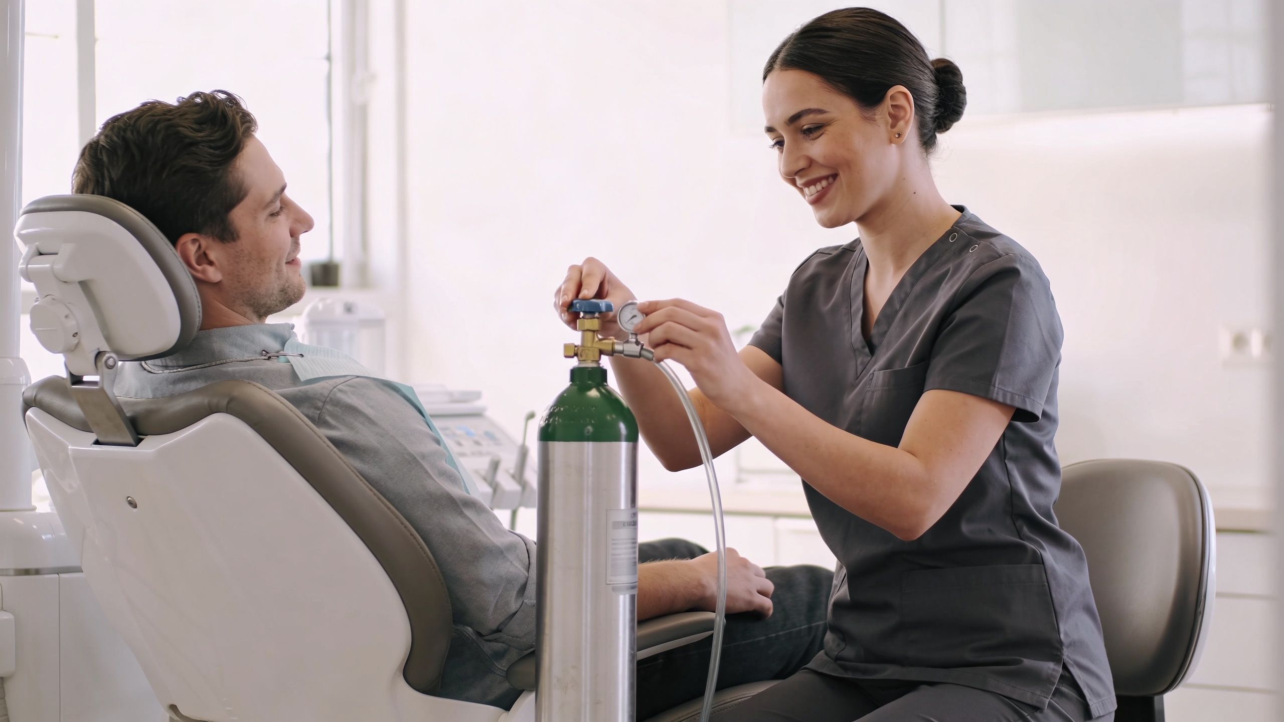 Relaxing Nitrous Oxide Sedation Dentistry in Bellaire, TX 2 A female dental assistant adjusting a nitrous oxide sedation tank for a male patient in a dental clinic.